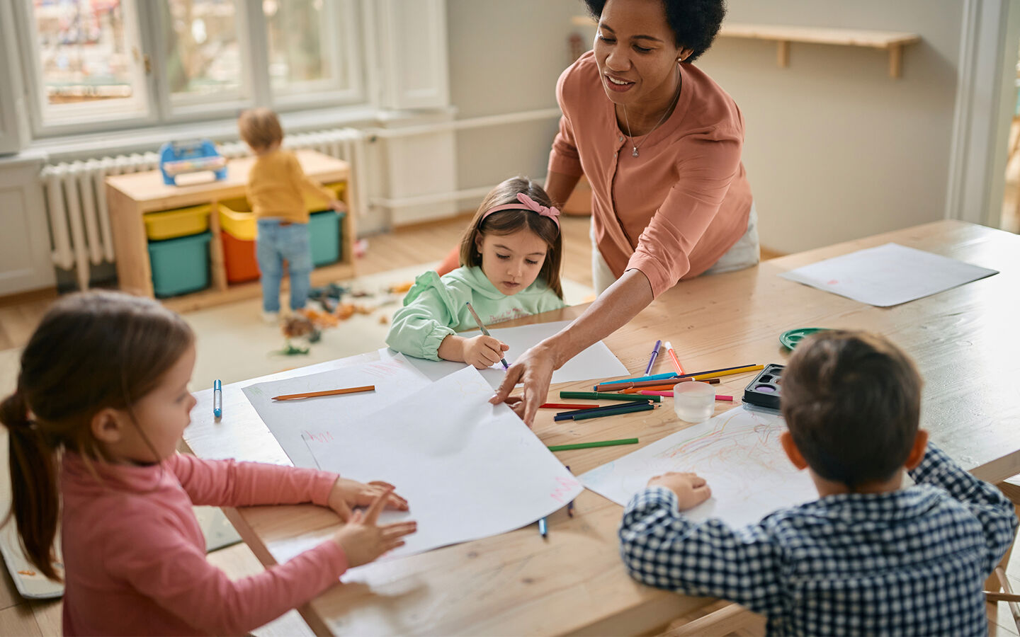 Une maîtresse fait du coloriage avec trois enfants